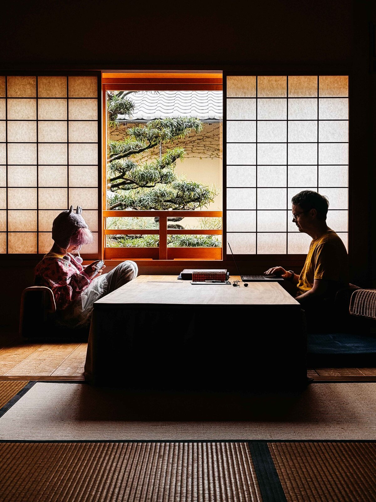 Father and teenage child playing on their computer devices at a traditional Japanese ryokan.