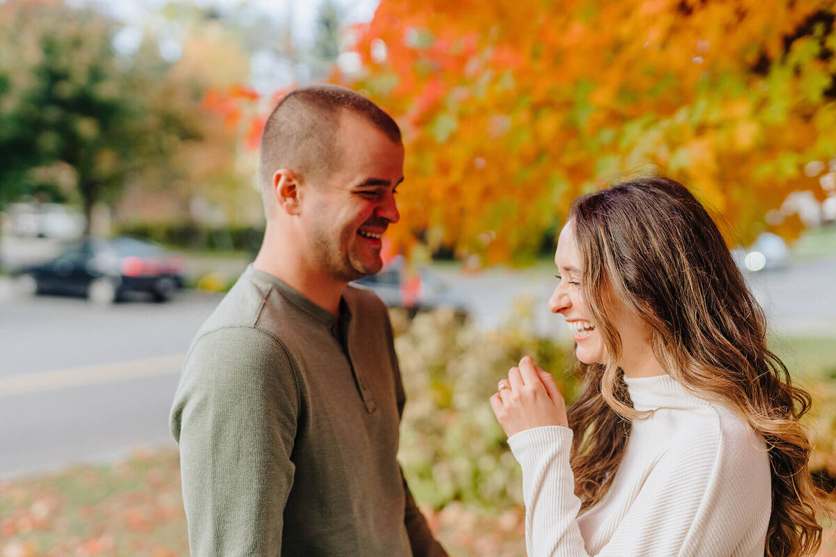 Couple looking at each other standing in front of an orange tree at Finger Lakes engagement session