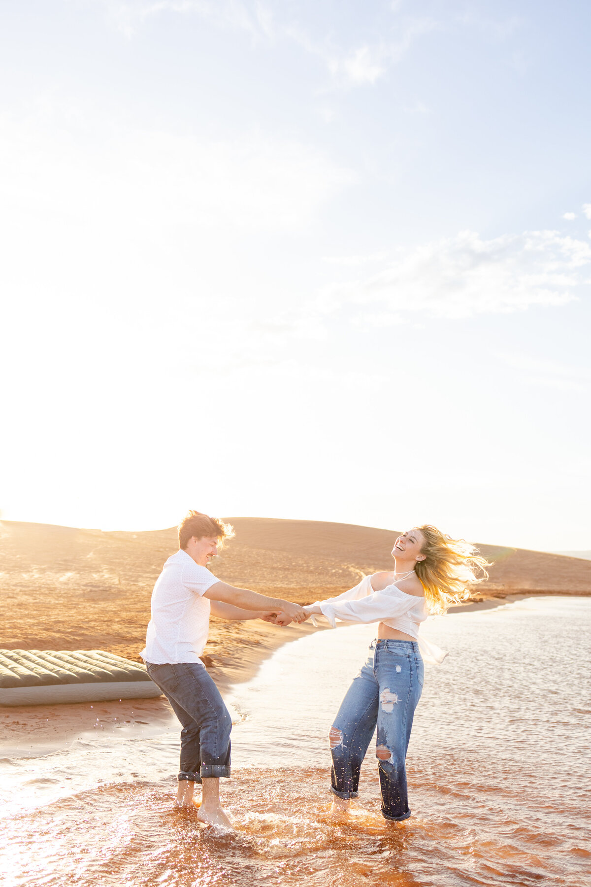 The boy and girl hold hands while laughing and spinning around in the water.