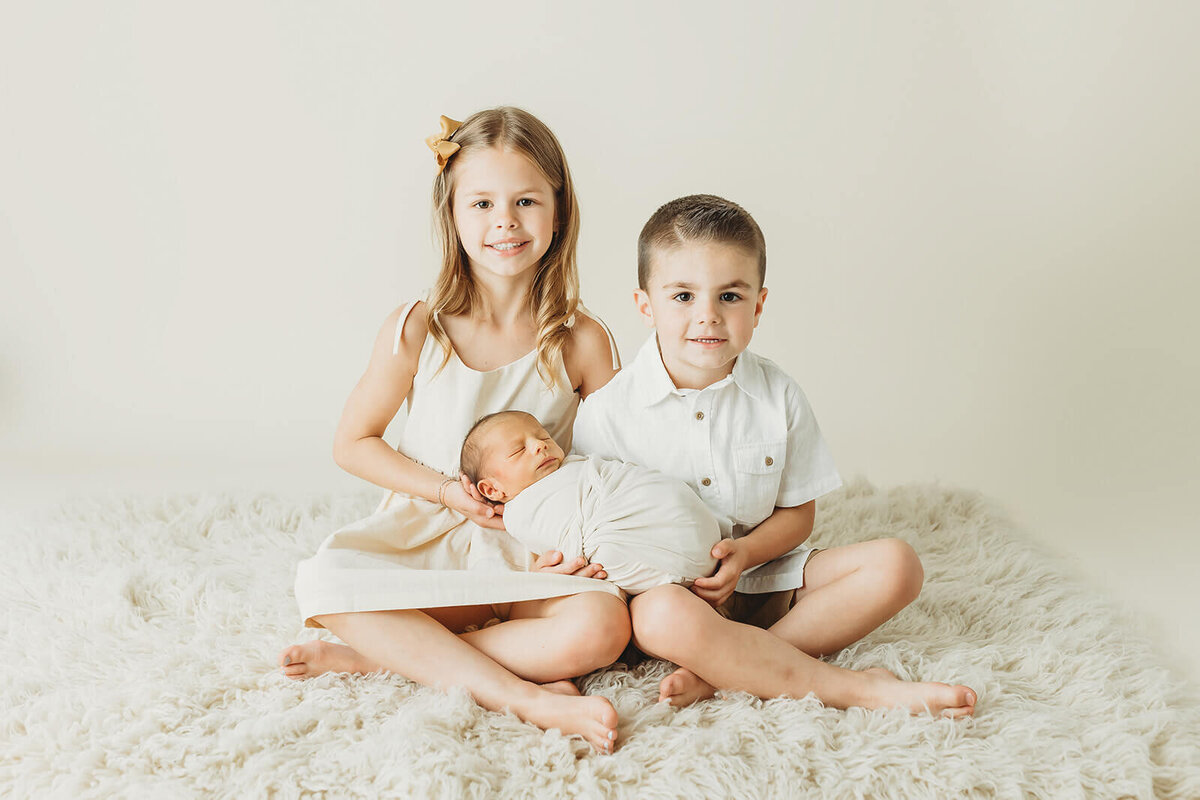 brother and sister holding their swaddled newborn baby brother in their york pa newborn session