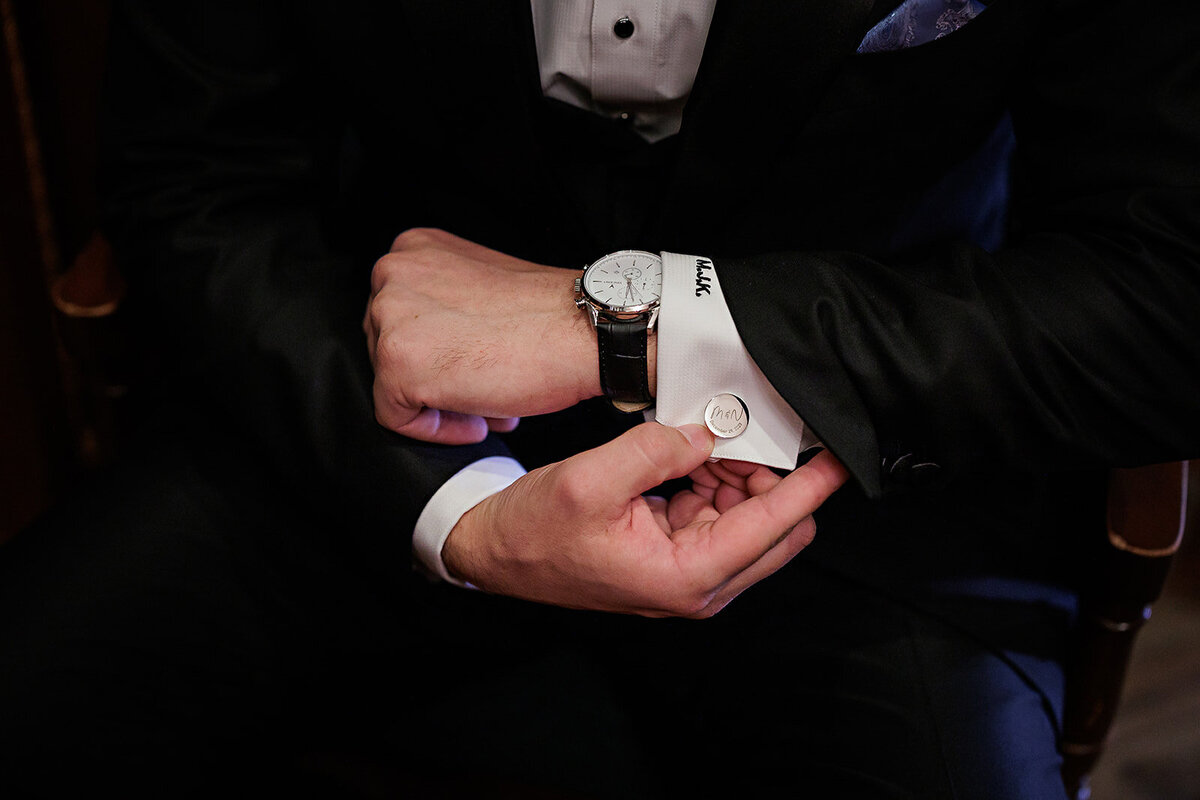 A closeup of a groom adjusts his cuffs on his wedding day.