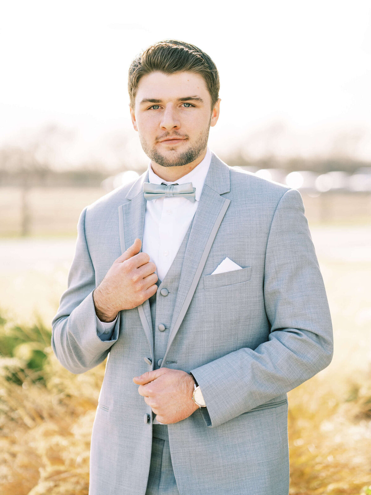 Groom dressed in light grey three piece suit stands outside before Denton, Texas wedding