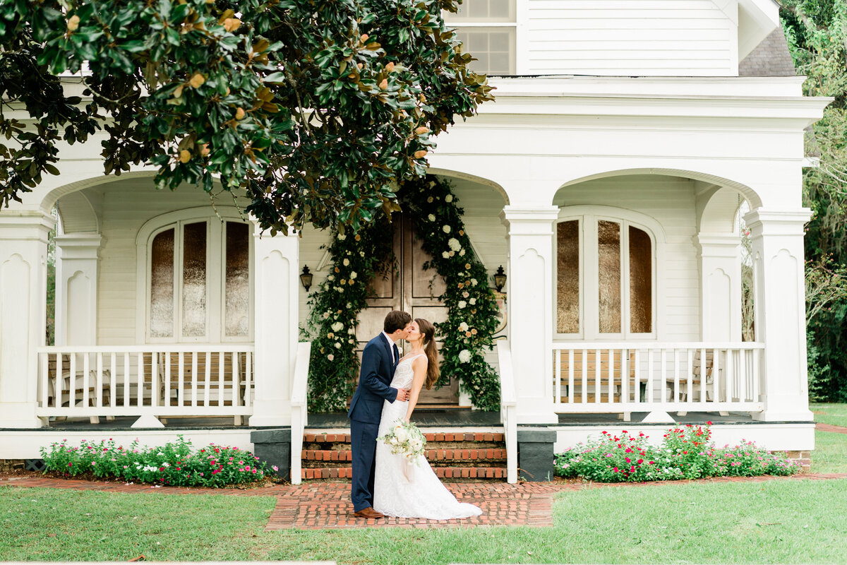 Bride and groom posing in front of historic house in Alabama