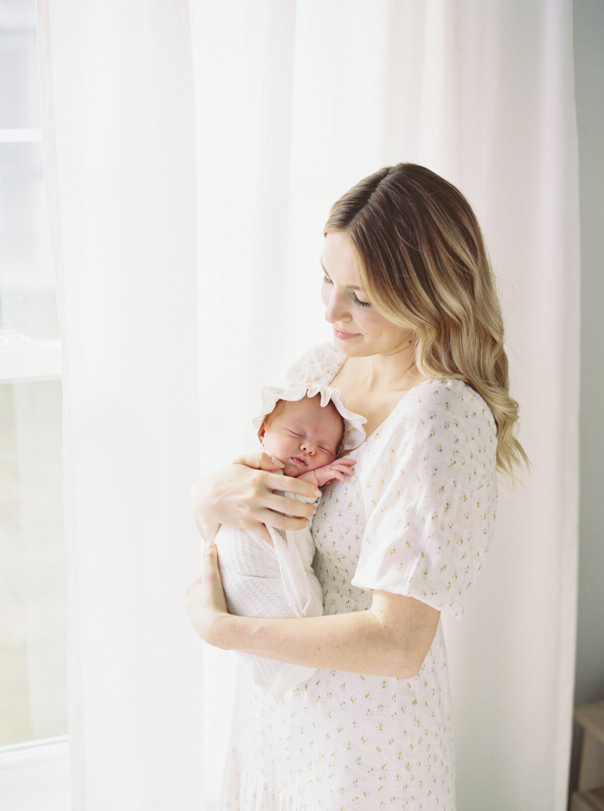 mother in master bedroom holding new baby girl by photographer in madison wi talia laird photography