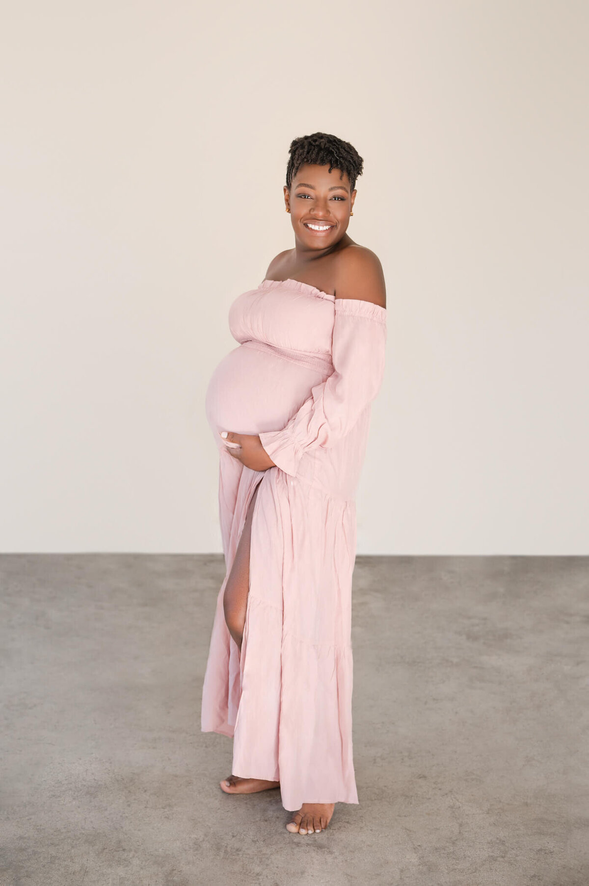 Woman standing to the side, smiling, and holding her pregnant belly