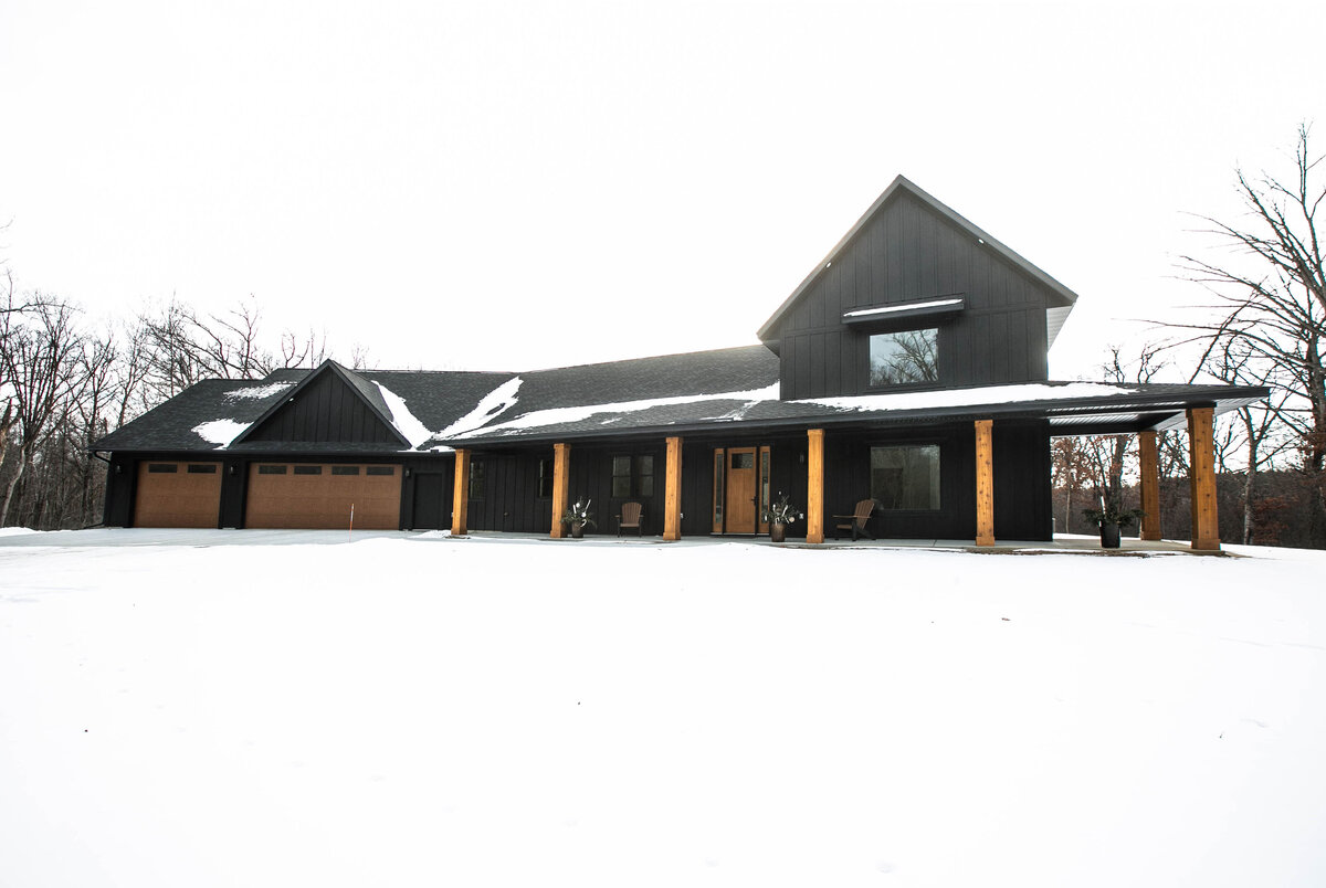 Exterior view of custom home in Elk River, Minnesota with black siding, wood details and front porch built by Cornerstone Custom Builds