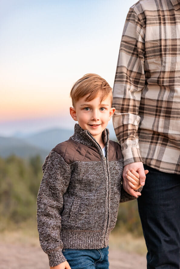 A boy hold his dads hand with mountains in the background.