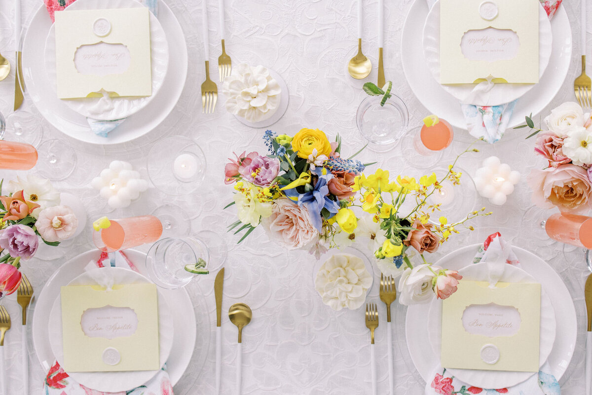 Aerial view of a table set for a meal with floral centerpieces, pastel-colored decor, place cards, white plates, gold cutlery, and glasses of a pink drink—as perfect as weddings in Banff Alberta.
