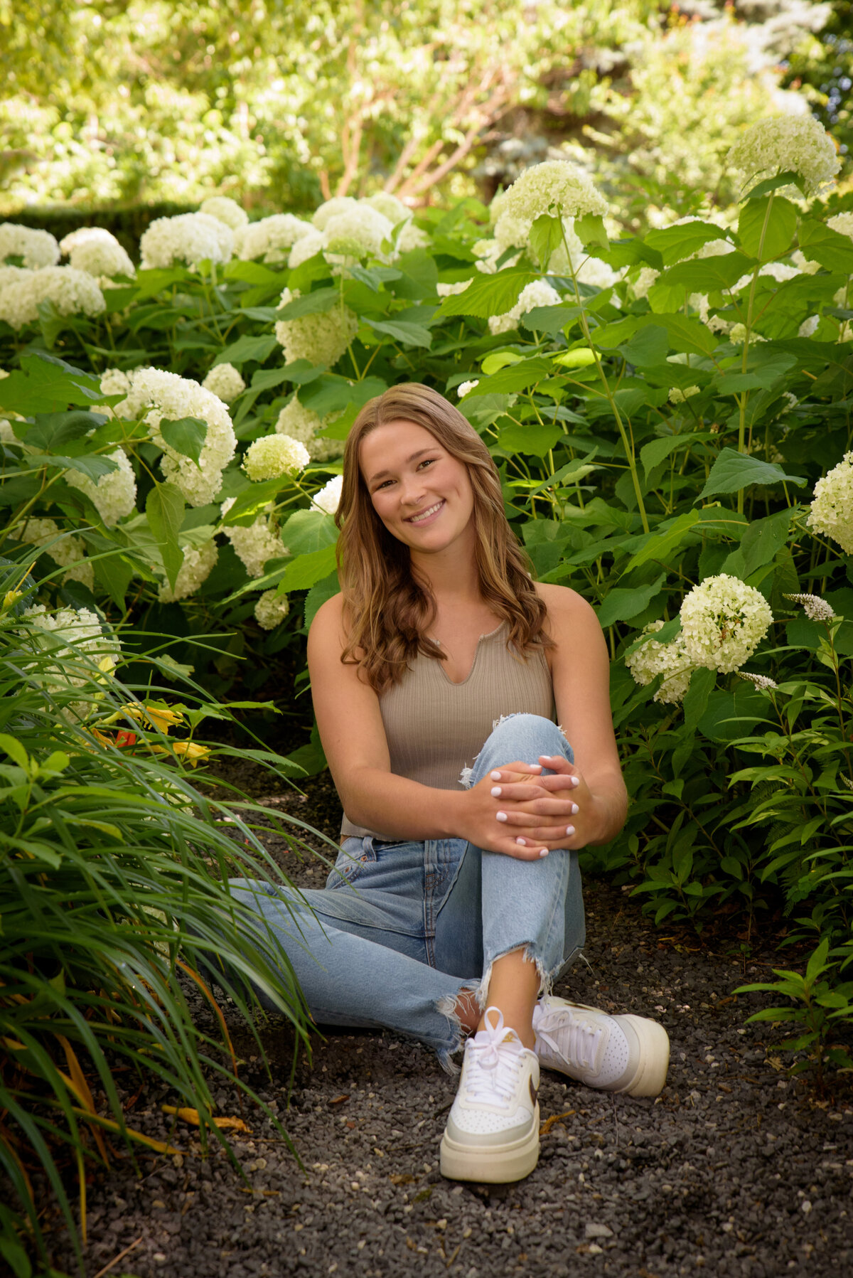 Luxemburg Casco High School senior girl wearing ripped jeans and a tan shirt sitting in flowers at the Green Bay Botanical Gardens in Green Bay, Wisconsin