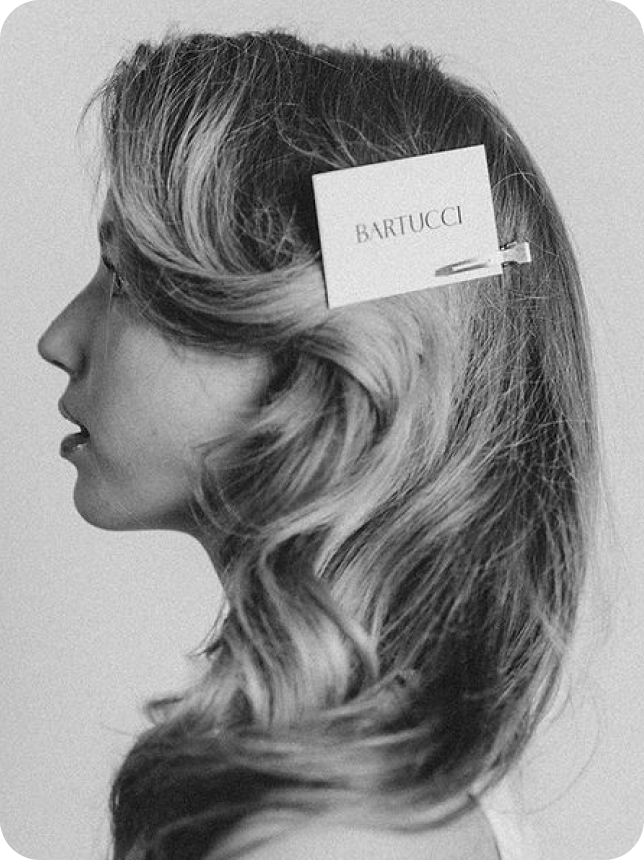 Woman with a bouncy blowout with a salon's business card clipped into her hair creatively to showcase their brand through socials. 