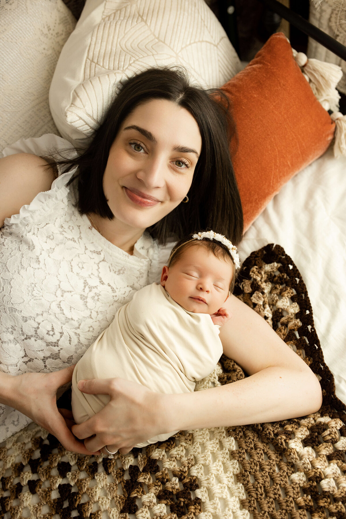 mom laying on a bed holding her swaddled newborn baby girl smiling at the camera