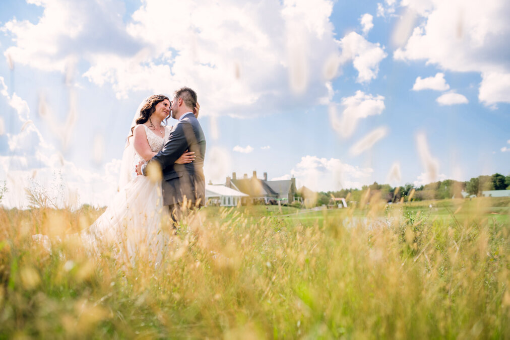 A bride and groom embrace in a field of tall grass.