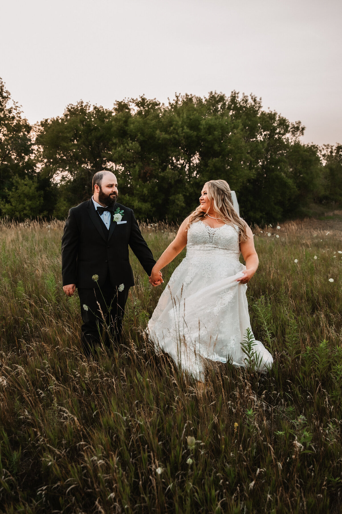 bride and groom hold hands and walk through field