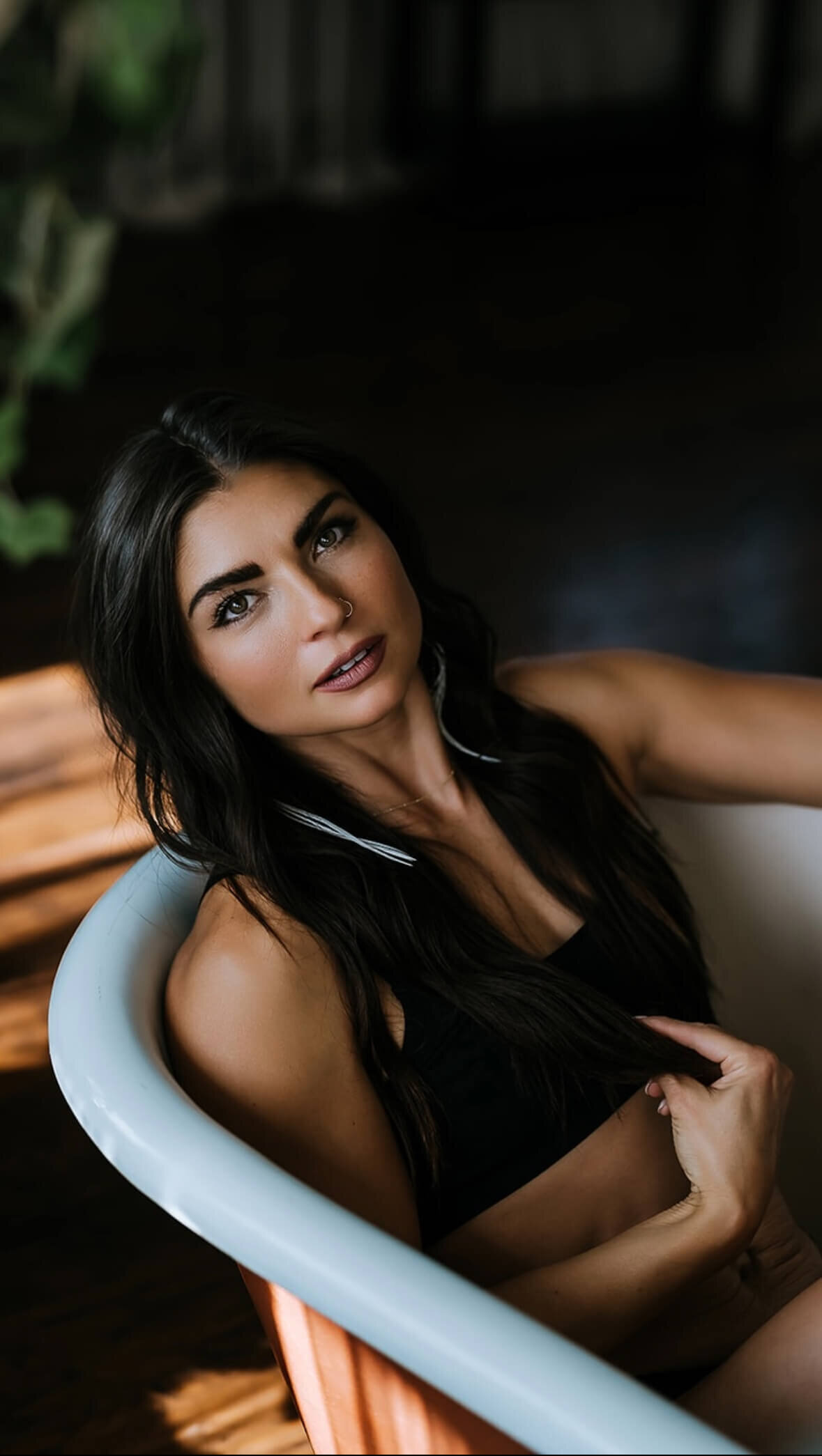 Boudoir image of a woman in a bathtub wearing black lingerie and feather earrings