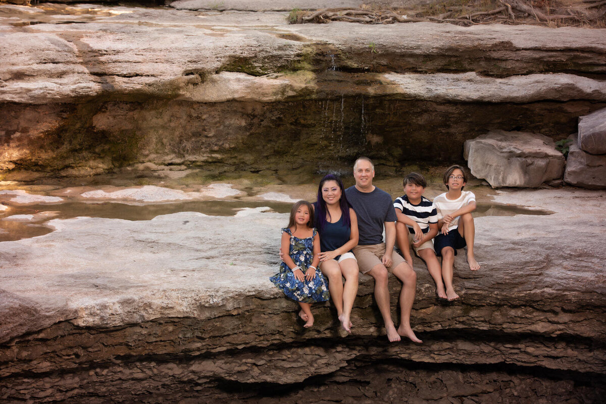 family-sitting-on-rock-legdge-at-airfield-falls-fort-worth-wearing-blues-and-tans