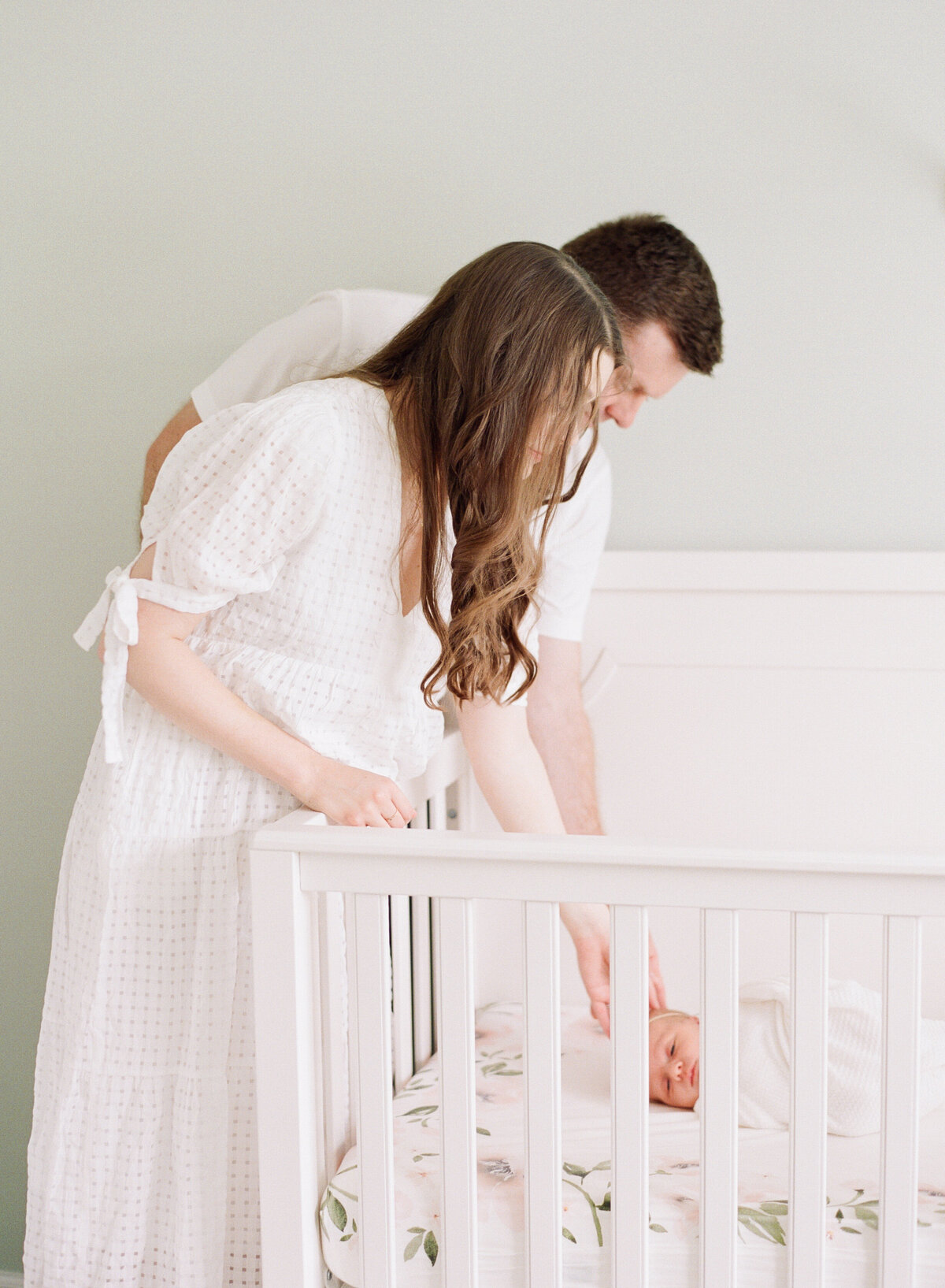 New parents reach into the crib to comfort their baby. Image by Raleigh newborn photographer A.J. Dunlap Photography.