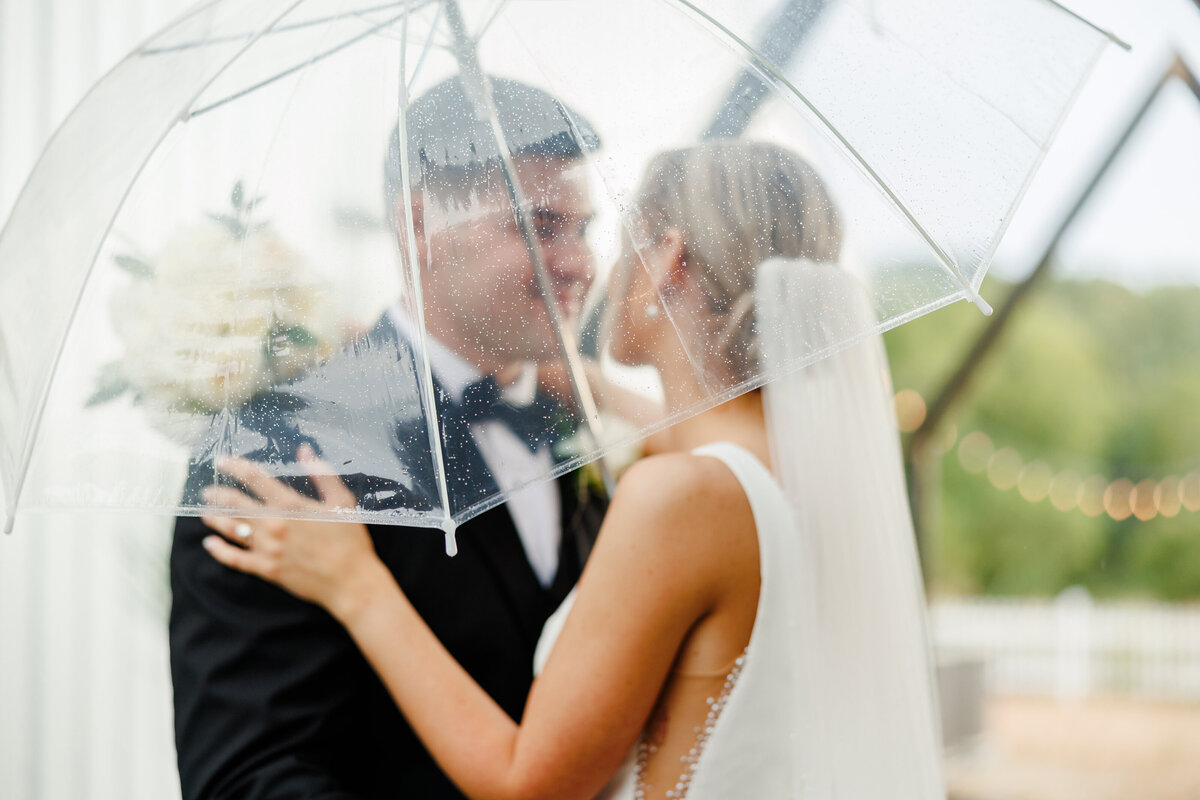 The bride and groom under a clear umbrella.