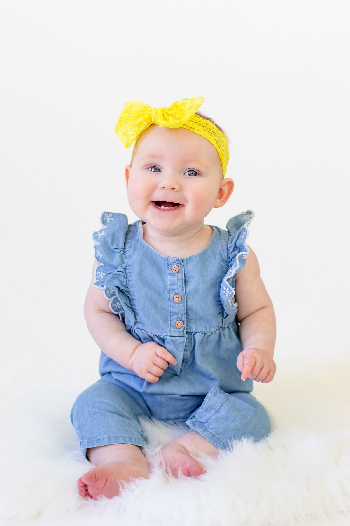 Six month baby girl in jean romper with yellow bow giggling