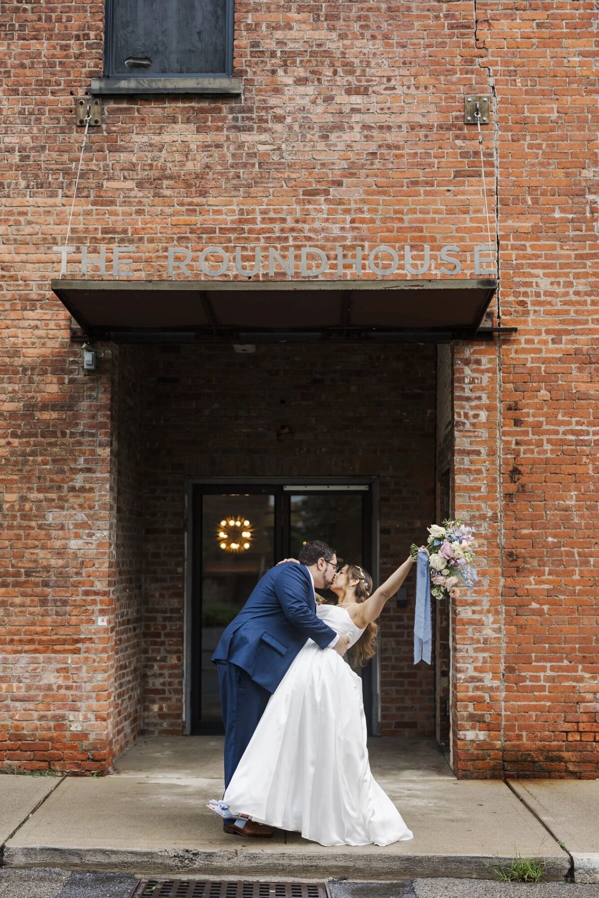 Bride and groom kiss and dip under The Roundhouse hotel sign on Beacon's Main Street