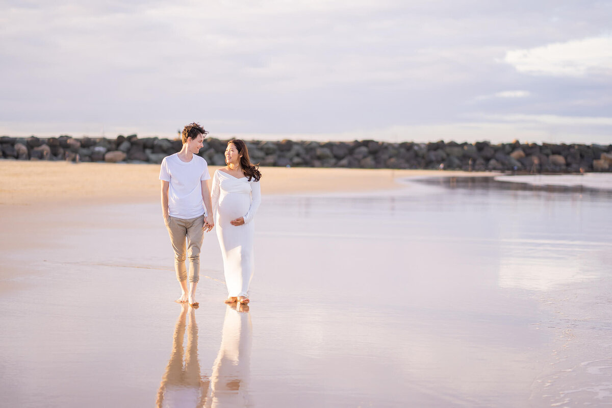 Couple running on the beach in purple sunset during maternity session in Gold Coast