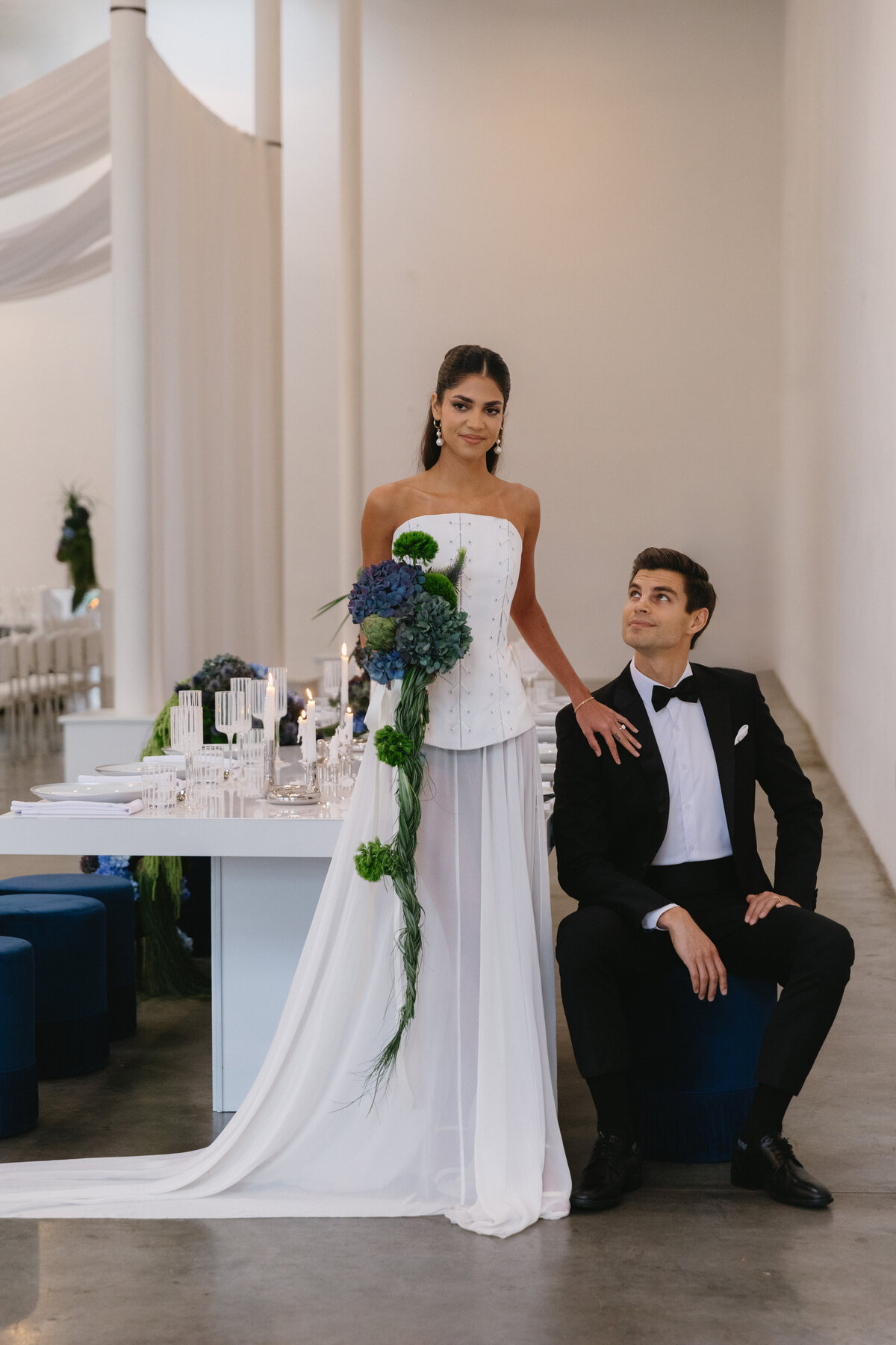 Bride and groom posed in a modern wedding venue with sculptural florals and soft neutral tones.