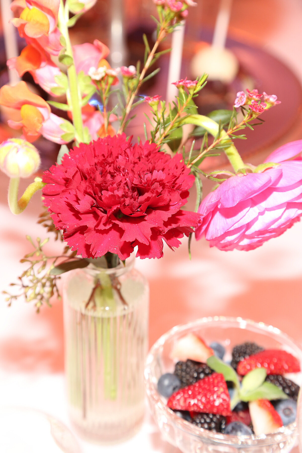 Close-up of a pink and red floral centerpiece in a glass vase with soft focus on luncheon setting.