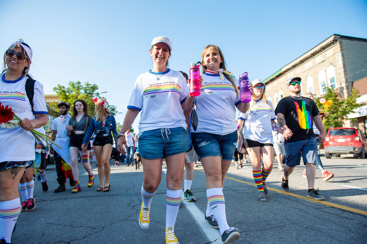 2 marchers in the Tweed Canopy Growth pride parade smiling at the camera as they walk by.  Captured by Ottawa Event Photographer JEMMAN Photography COMMERCIAL