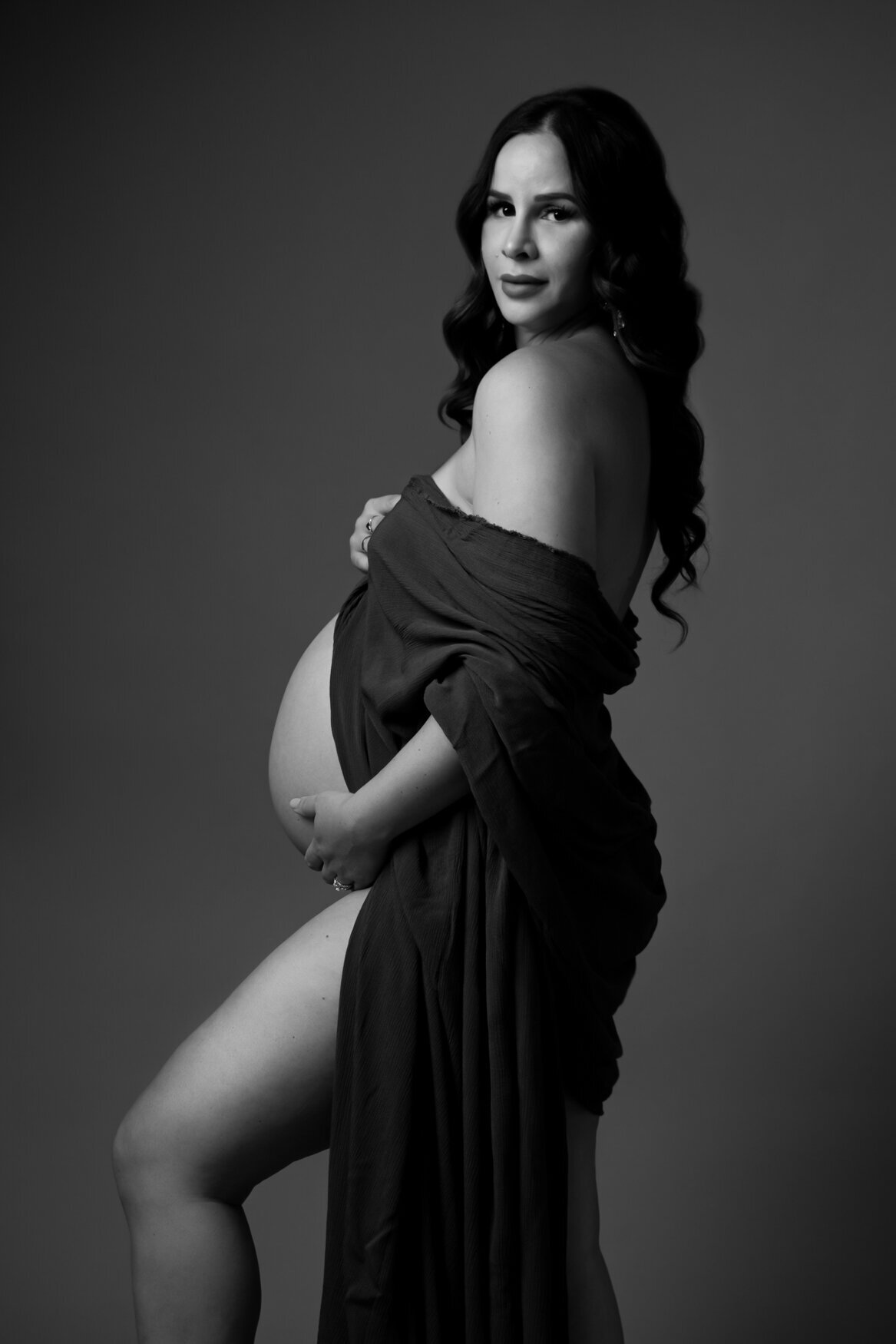 A portrait of a pregnant woman covering her body only with a dark fabric showing her belly and legs