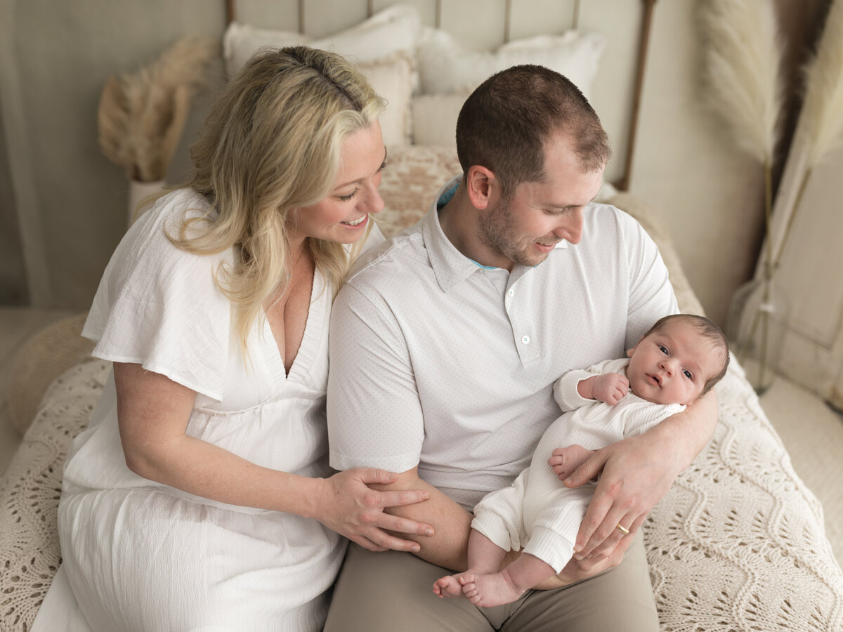 mom and dad holding newborn baby boy in white onesie for studio lifestyle session cleveland newborn photographer