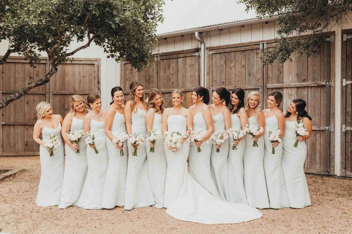 bridesmaids look at bride and smile while she looks at allyson blankenburg for her wedding photography