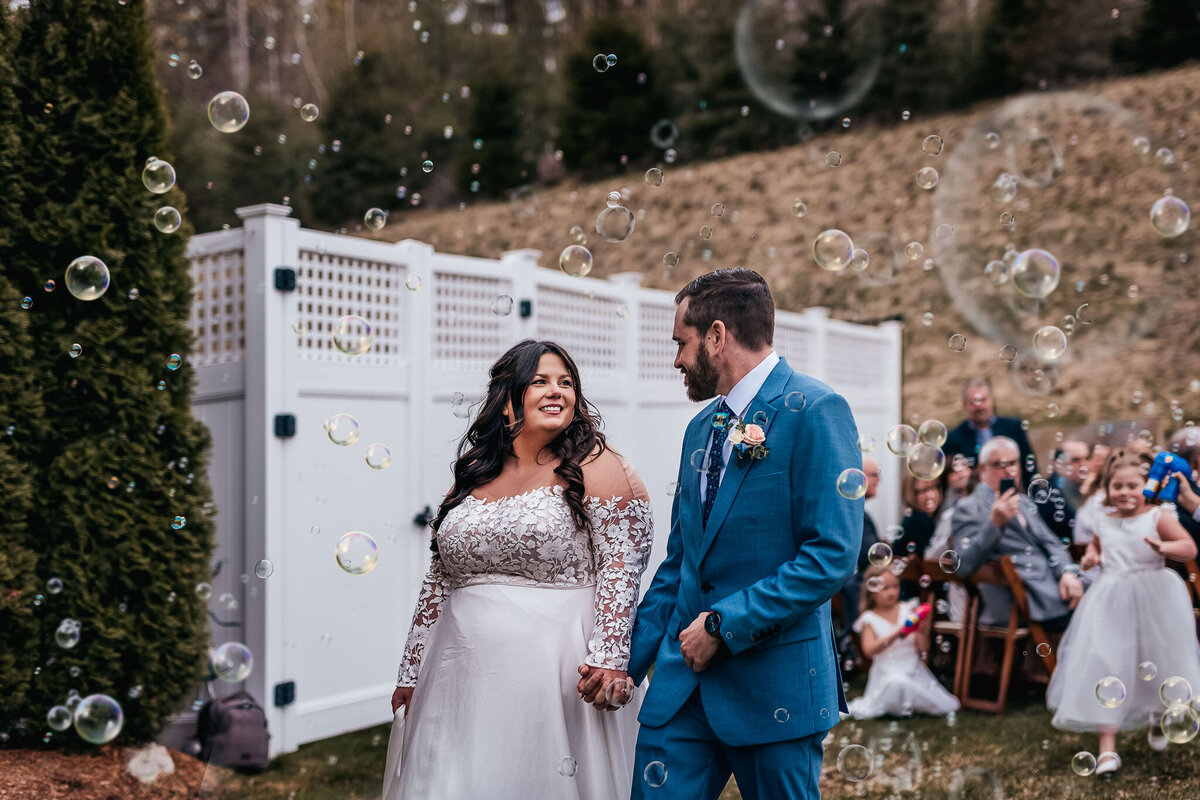 Bride and groom exit down the aisle while guest blow bubbles in beautiful spring wedding at Bedford Village Inn in Bedford NH by Lisa Smith Photography