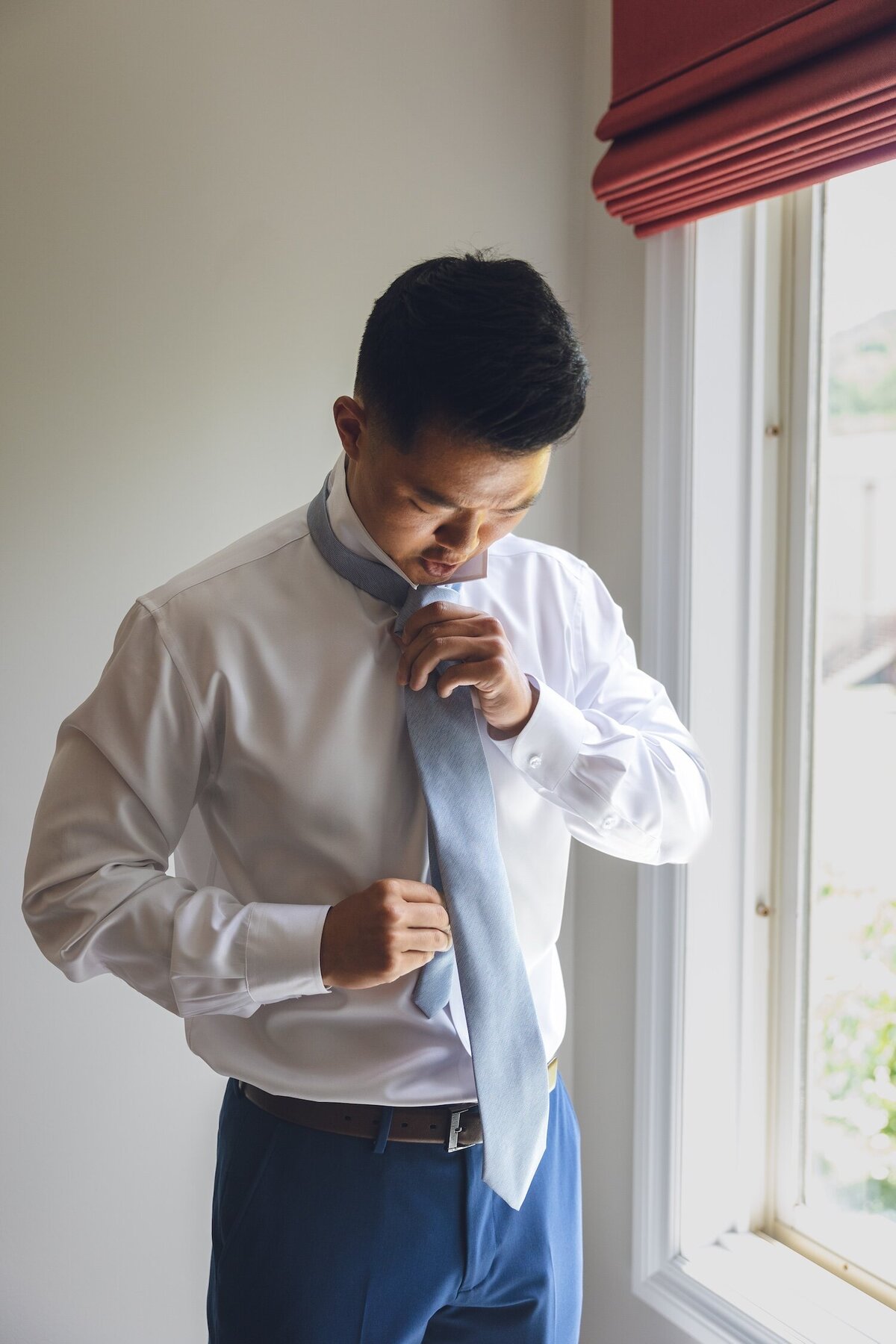 Groom adjusting his tie in window light at Crystal Springs Resort