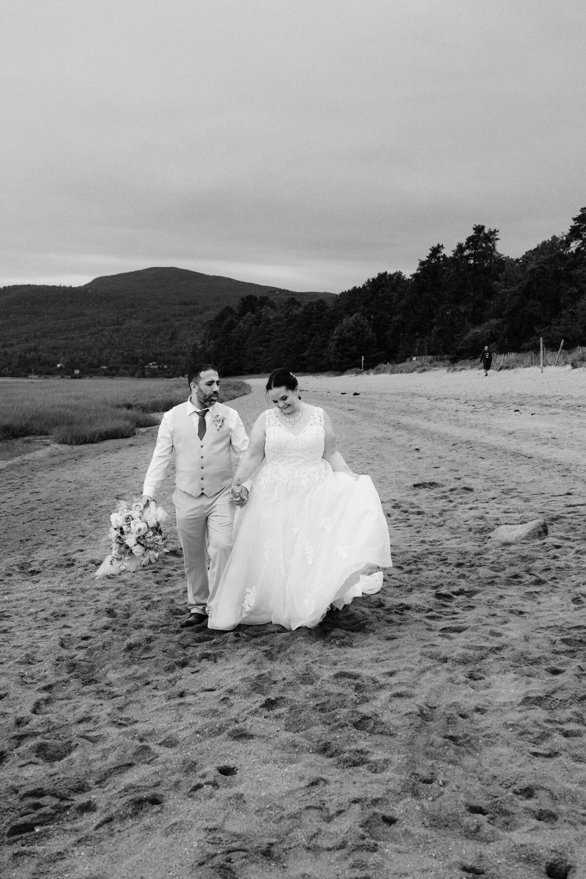 black and white image of a bride and groom walking on a beach