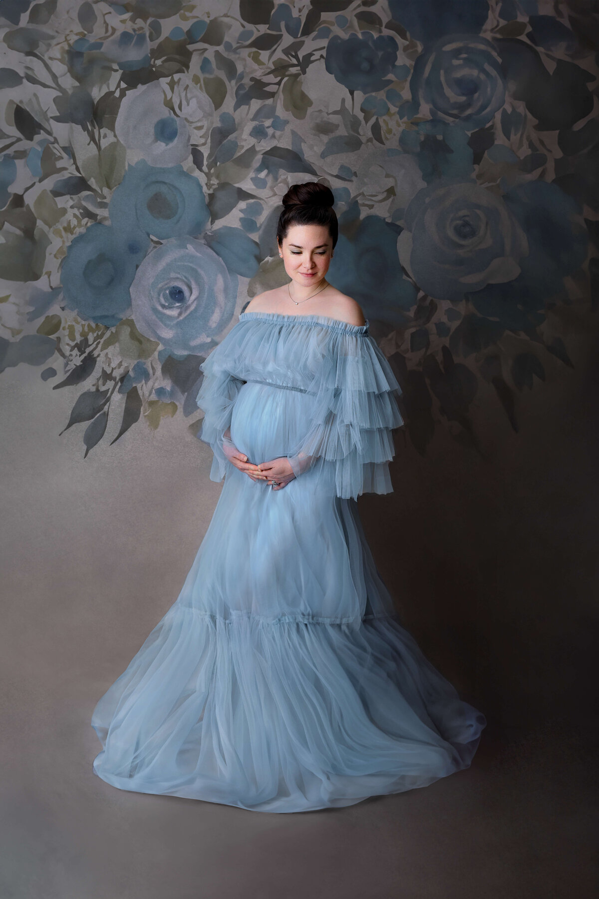 expecting mother wearing a blue maternity gown on a floral backdrop at her maternity sessioni