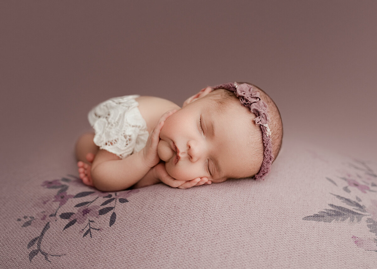 Baby newborn in falling froggy pose on purple