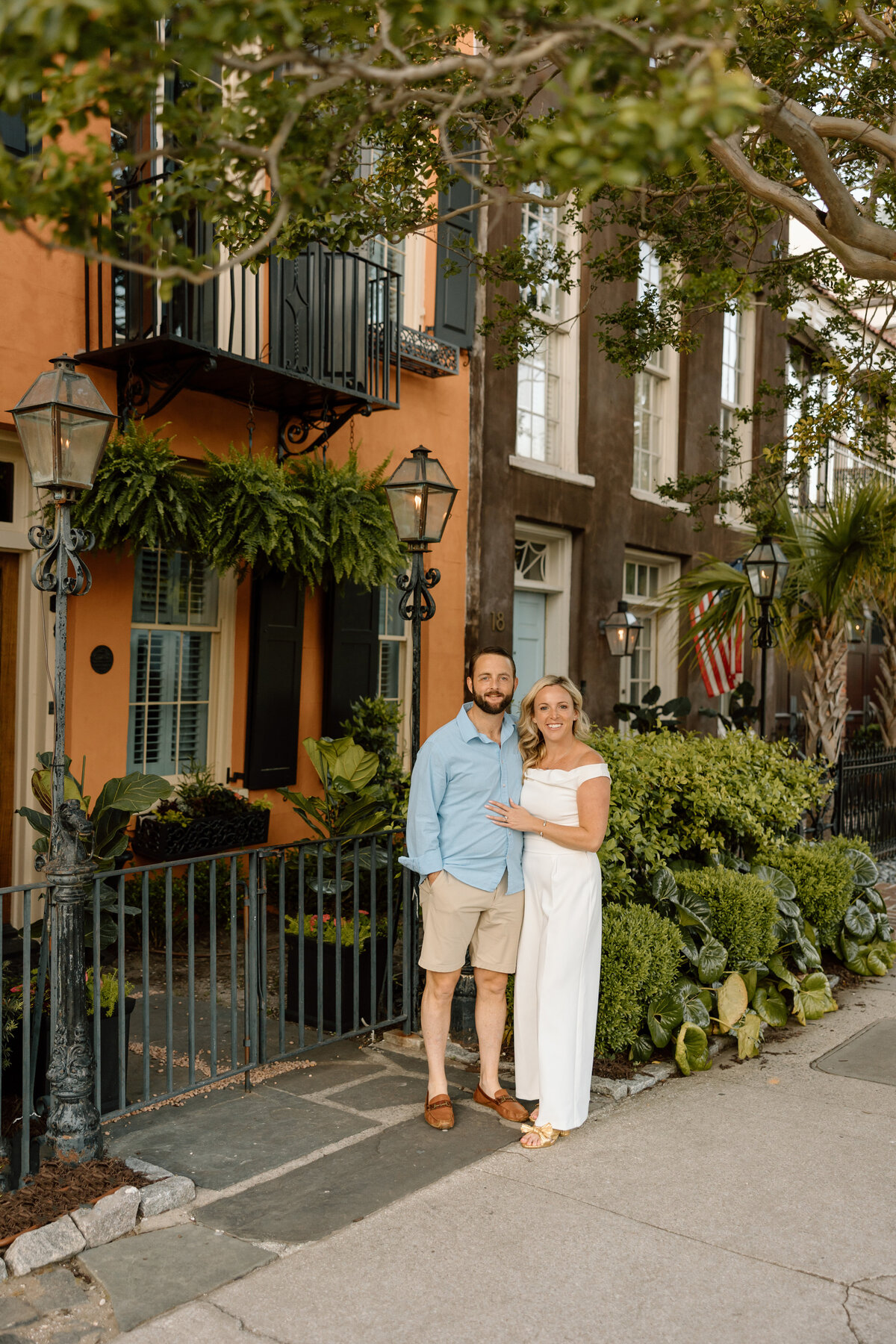 Engaged couple standing in front of colorful historic homes during a downtown Charleston engagement session on Rainbow Row.