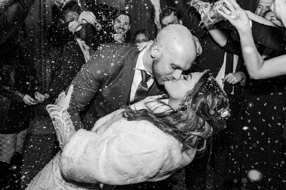 Bride and groom kissing as it snows and guests cheer