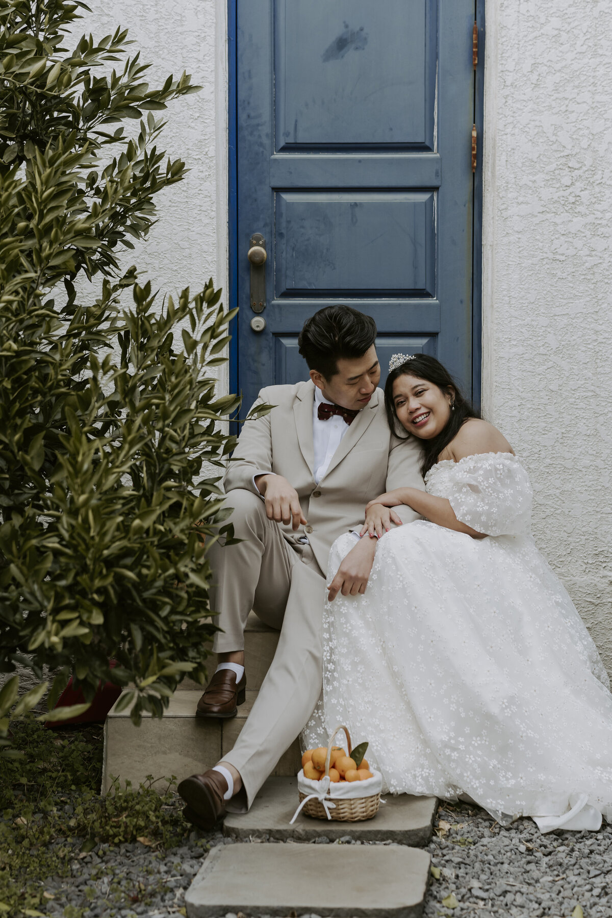 the couple sits down in front of a blue door the bride leaning her head to the groom's shoulder