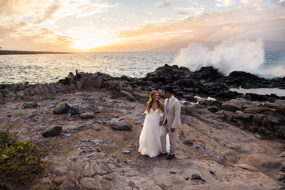 Bride and groom walking on the beach at sunset.