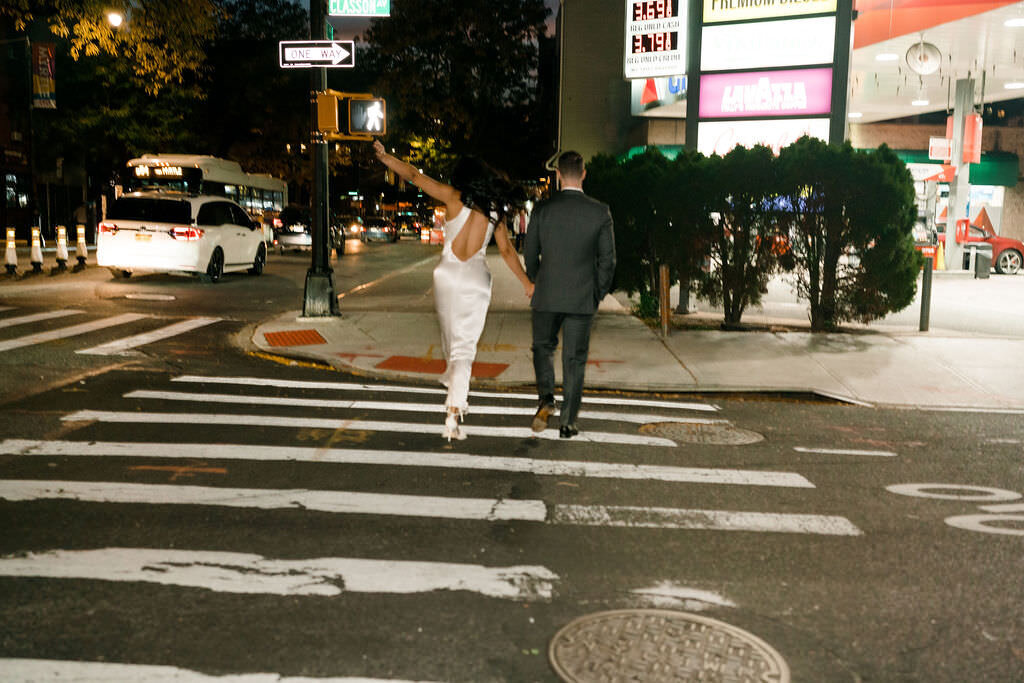 bride and groom walking across a city street holding hands
