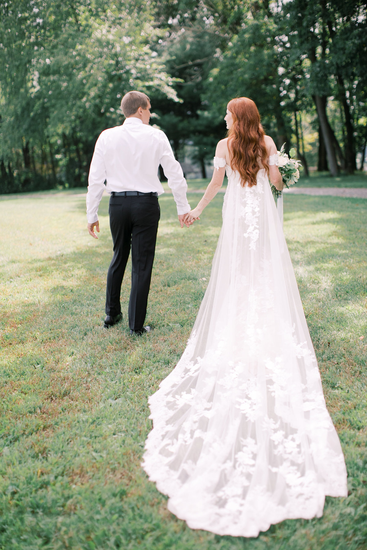 bride and groom holding hands walking through grassy field