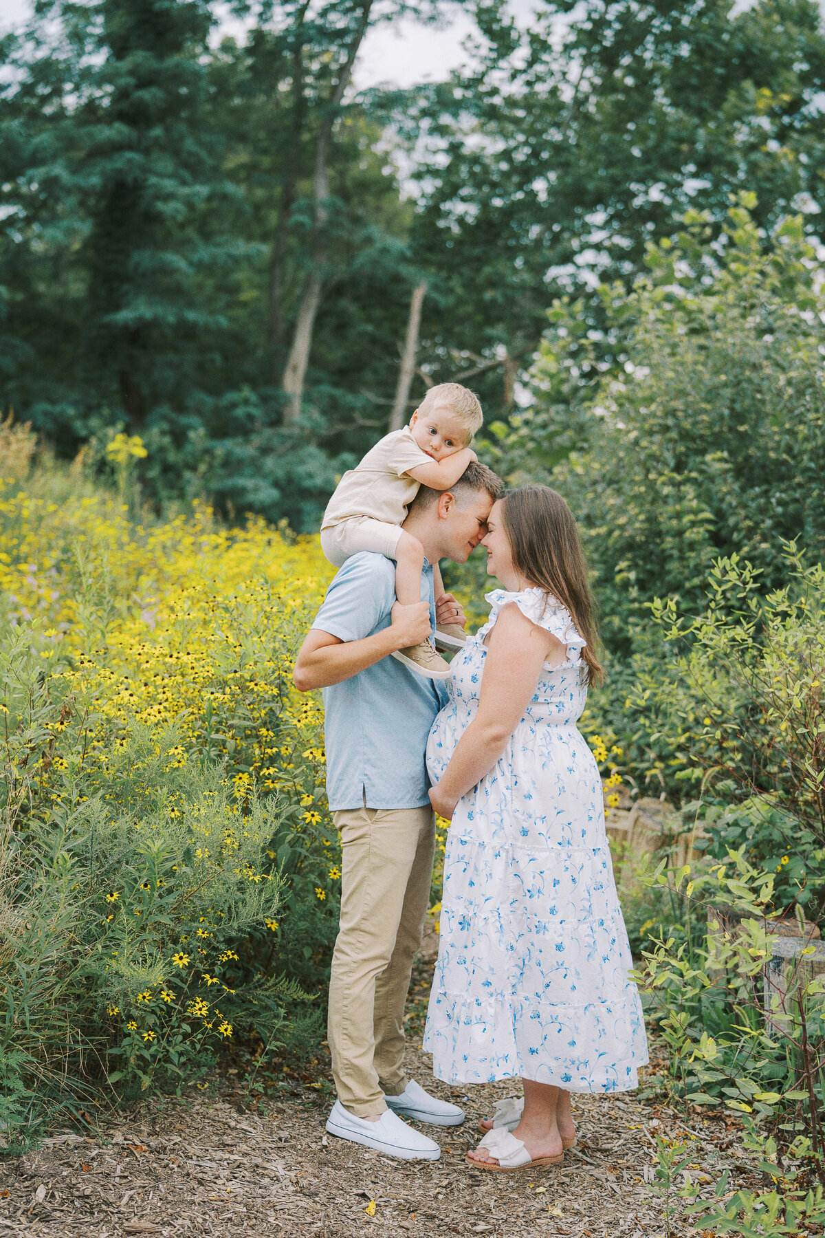 mom and dad resting heads with little boy on dad's shoulders during maternity photos