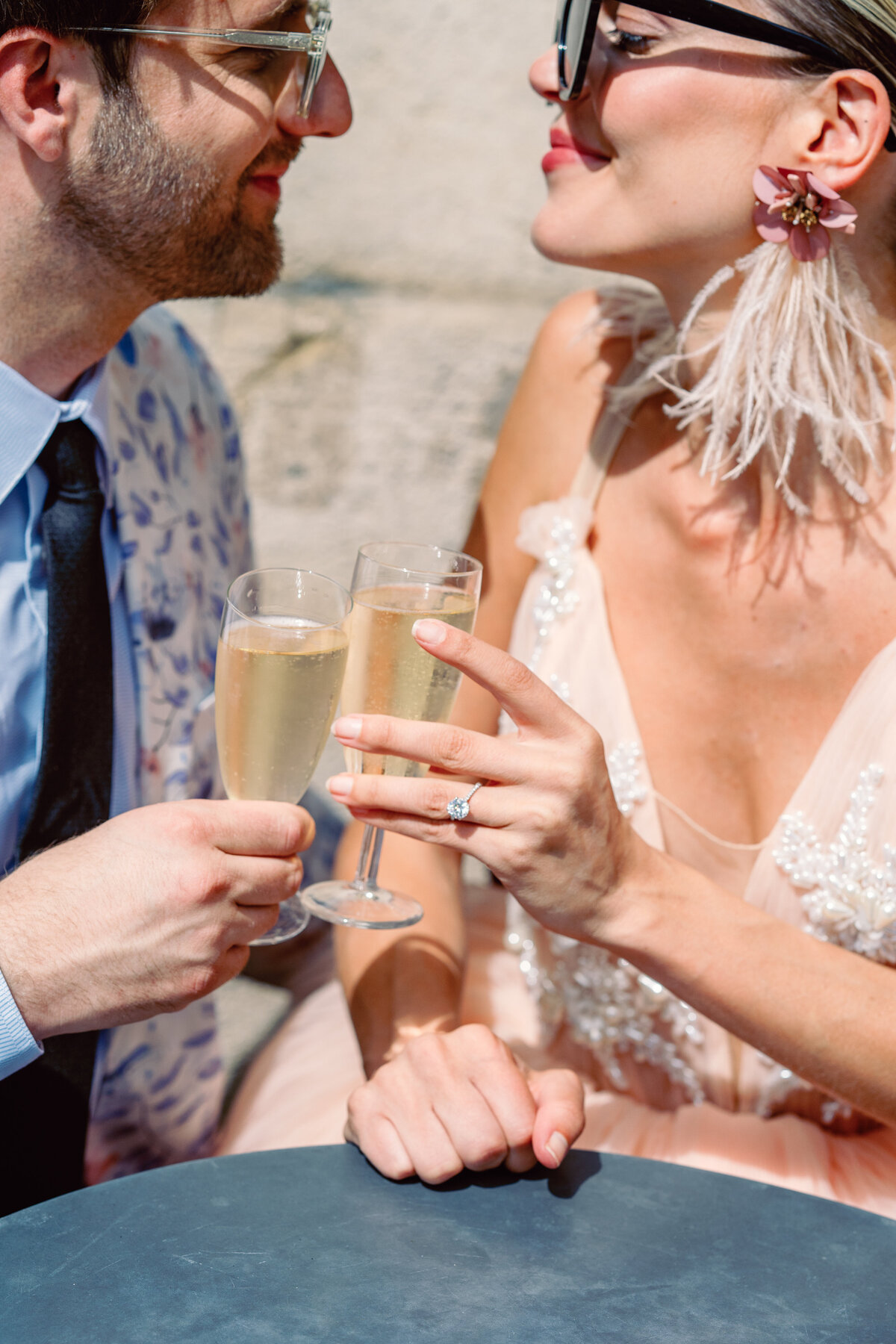 Couple at a cafe enjoying champagne, she in a peach gown with long train at their Paris engagement session, photographed by Italy wedding photographer.