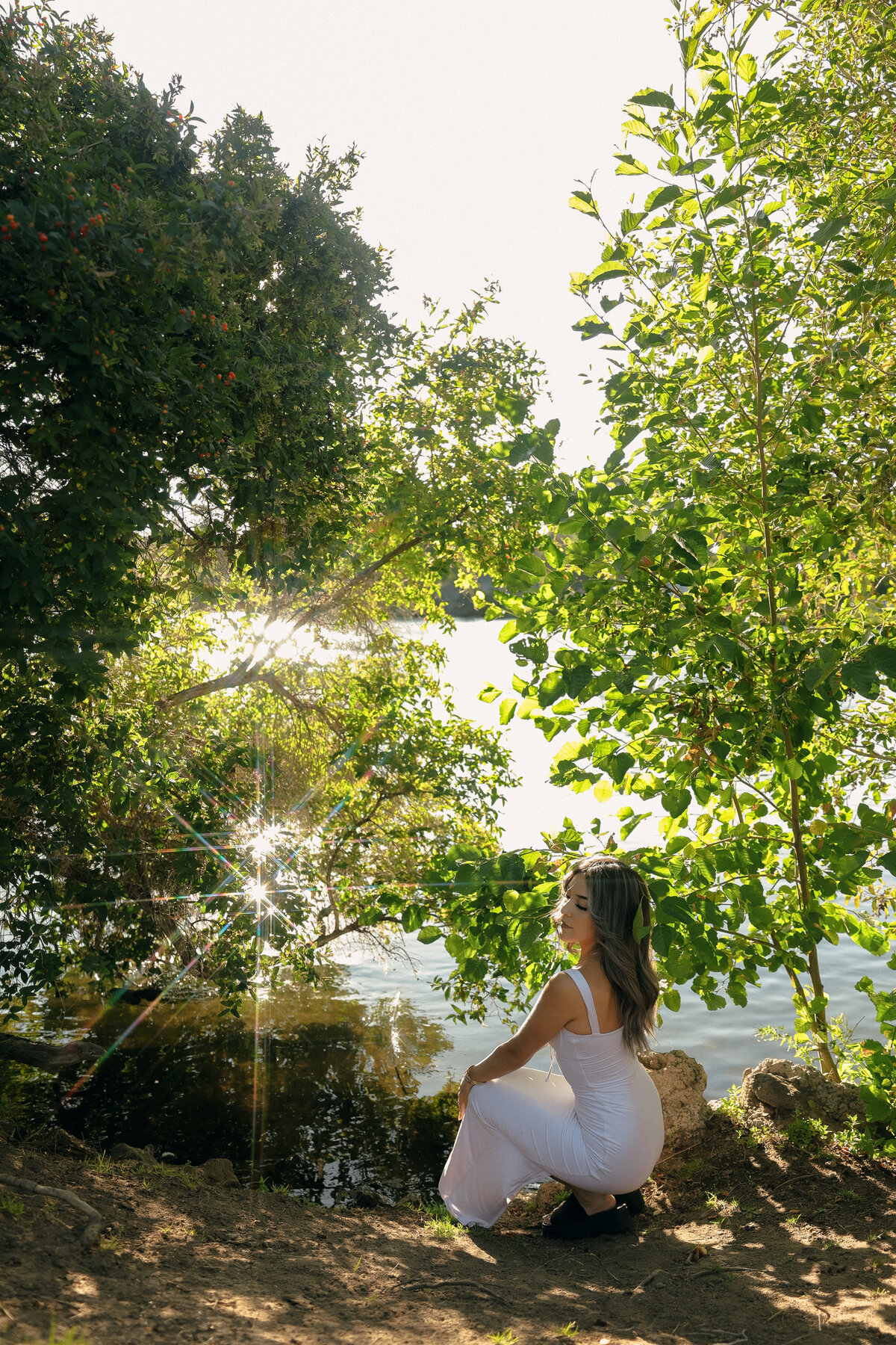 Senior Portrait of Girl in White Outfit Leaning Against Tree in Sunlit Forest Setting