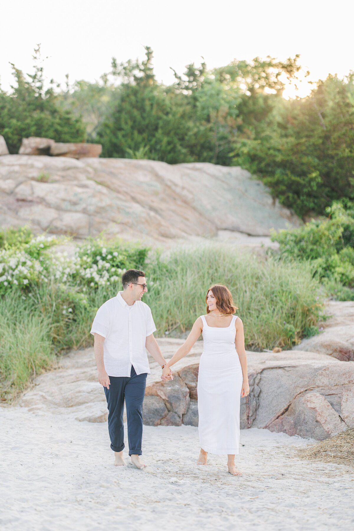 A couple holding hands and walking on Wingaersheek Beach representing a Gloucester engagement photographer's work.