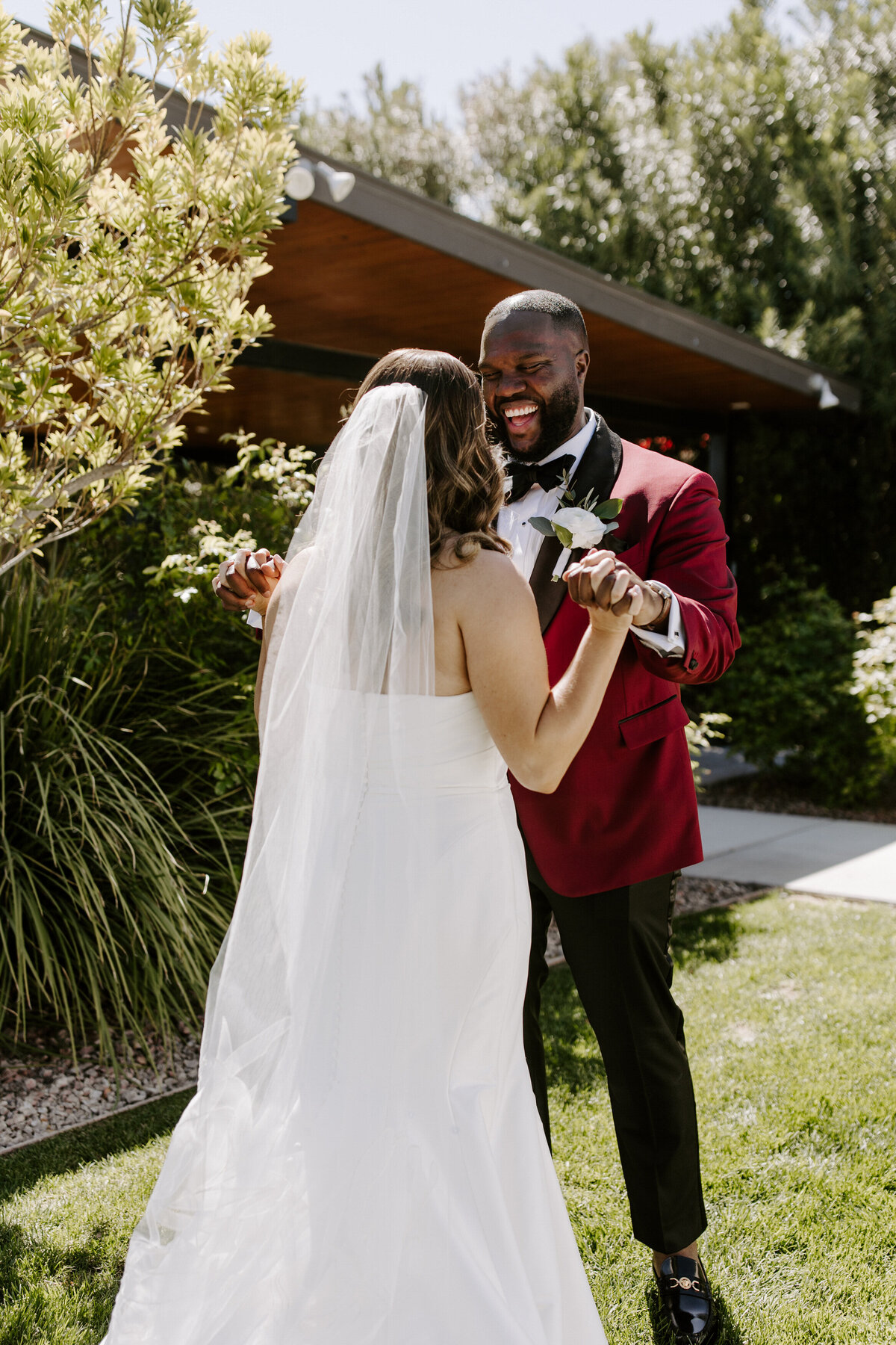 A couple smiles happily at one another while holding hands.