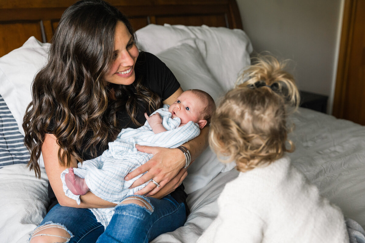 mom holding newborn baby with big sister in lifestyle Phoenix photography session