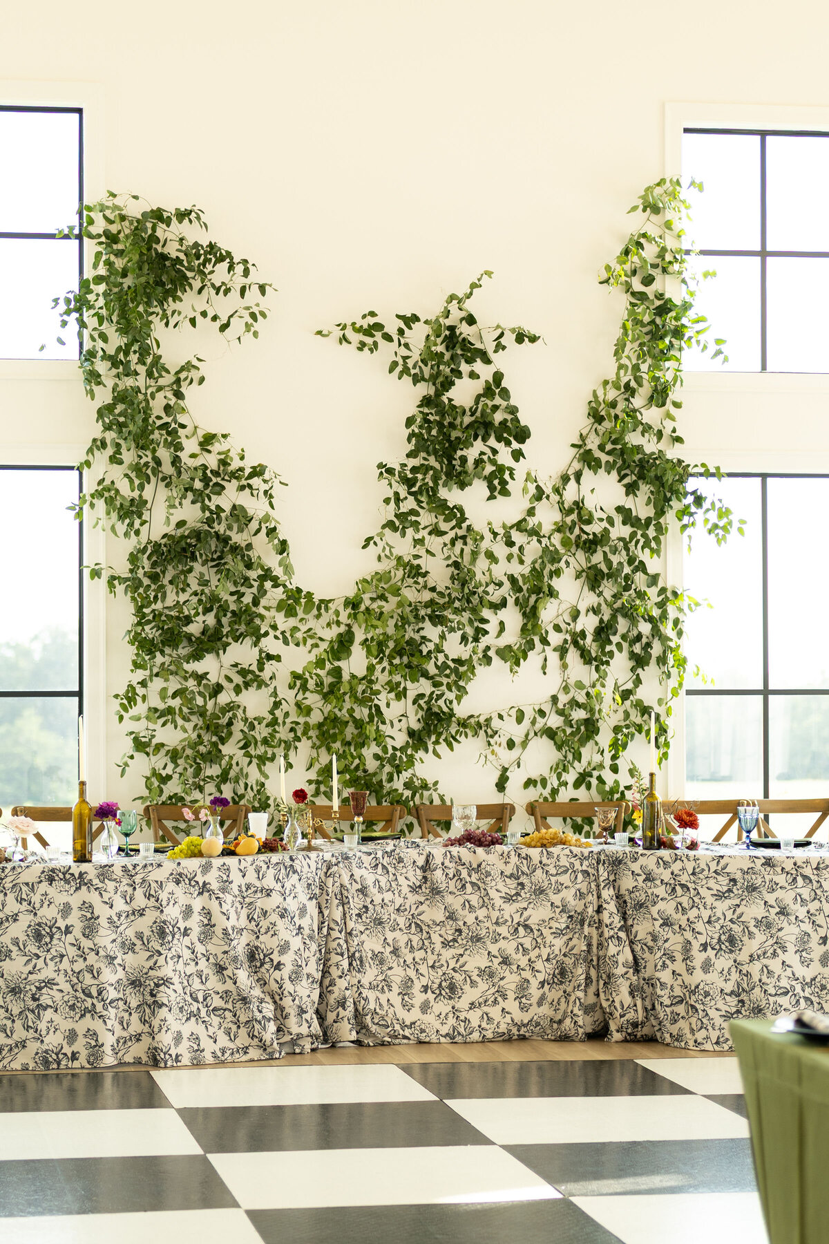 Greenery installation climbing the wall behind the wedding head table with black-and-white floral linens and colorful centerpiece arrangements.