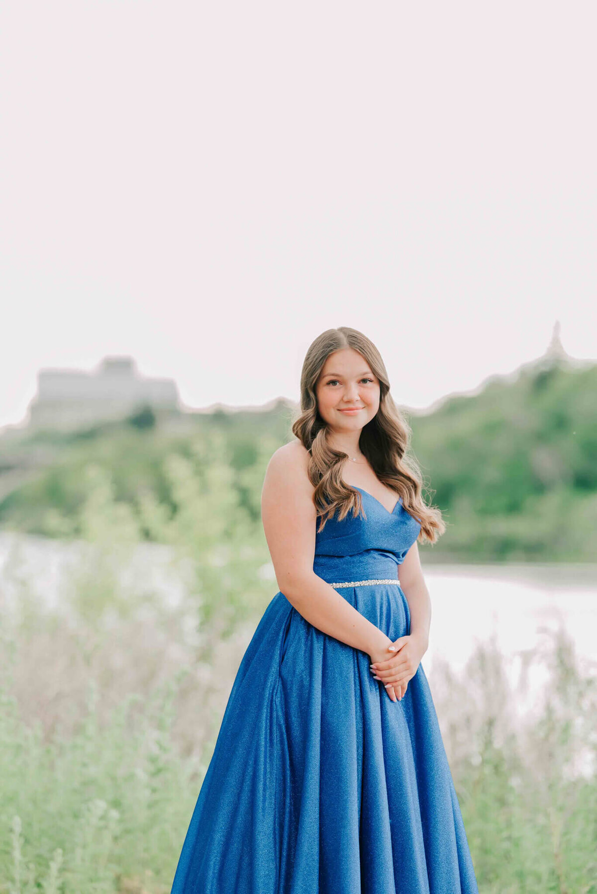 Pretty brunette in a blue dress standing by a river and trees.