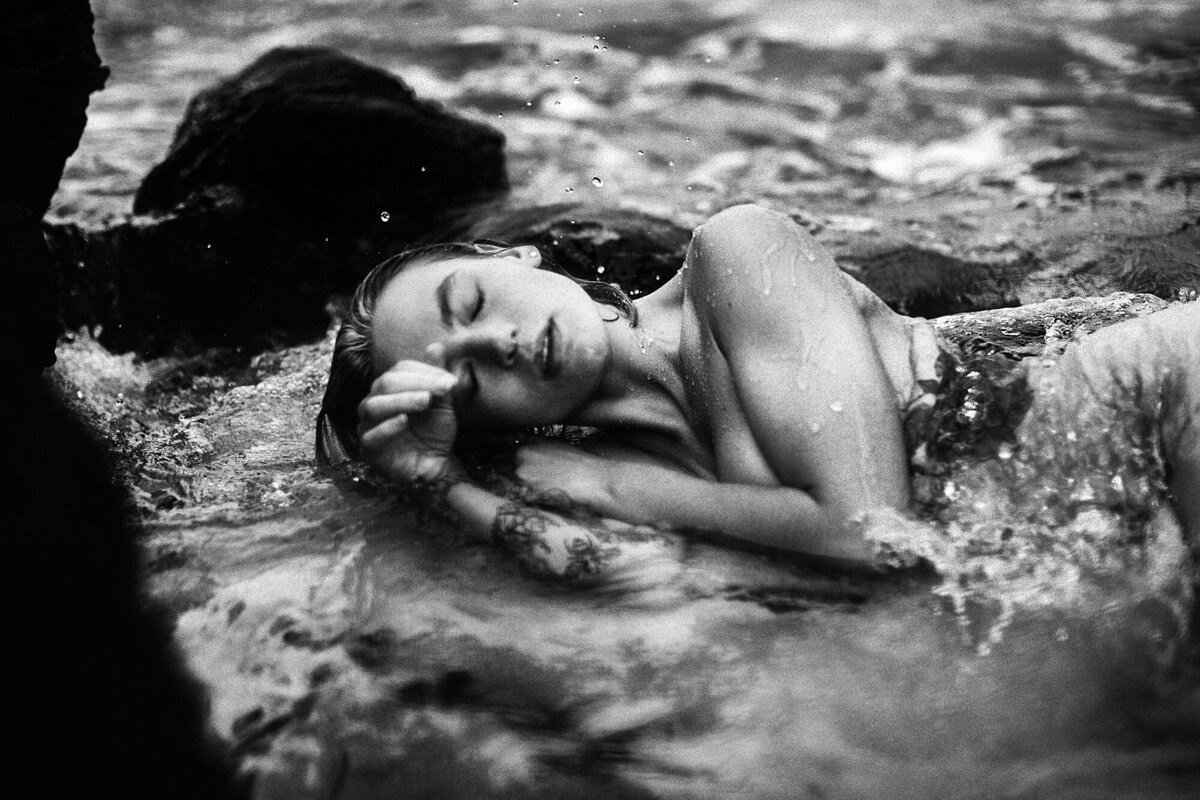black and white portrait of a woman laying in the water during her boudoir photoshoot on the beach